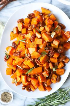 a white plate topped with sweet potatoes and pecans next to rosemary sprigs