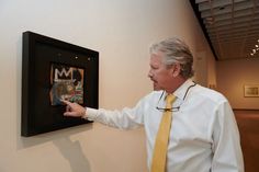 a man in a tie points at a framed photograph on the wall with his hand