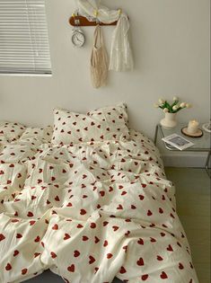 an unmade bed with red hearts on it in a bedroom next to a window