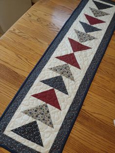 a quilted table runner with red, white and blue triangles on the border is sitting on a wooden table