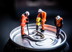 three figurines are standing on top of a soda can, one is holding a tool and the other is cleaning