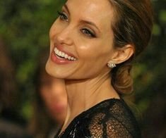 a woman in black dress smiling and looking at the camera with her hair pulled back