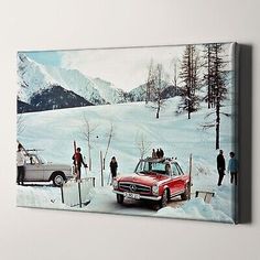 a red car parked in the snow with people standing around it and mountains in the background