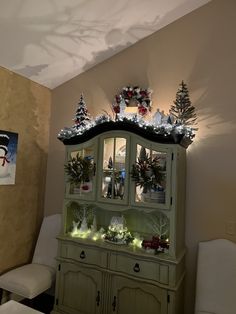 a green china cabinet with christmas decorations on it's top and lights around the top