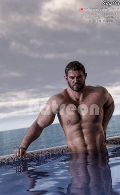 a man standing in the water with his shirt off and no shirt on, looking at the camera