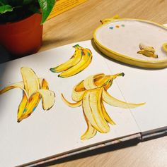 some bananas are on a table next to a potted plant and a drawing book