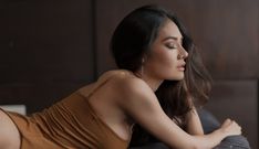 a woman laying on top of a bed in a brown dress