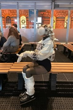 a woman sitting on top of a wooden bench in front of two benches with people standing around