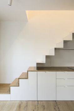 an empty kitchen with stairs leading up to the upper floor, and white cabinets below