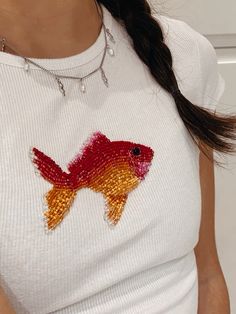 a woman wearing a white shirt with a red and yellow fish embroidered on the front