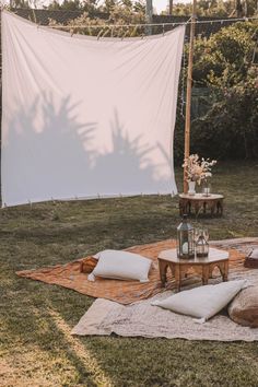 a white sheet is hanging over a table with pillows and vases on it in the grass