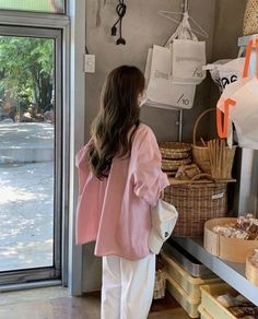 a woman standing in front of a store filled with baskets and breads next to a glass door