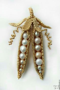 a brooch with pearls and gold beads on it's side, sitting on a white surface