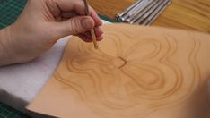 a person holding a pencil in their right hand as they work on a wood carving