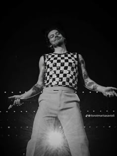 a man with tattoos on his arms and legs standing in front of a stage wearing a checkered shirt