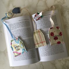 an open book with three pieces of fabric hanging from it's pages and two small tags attached to them