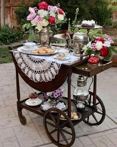 an old fashioned serving cart with flowers and tea cups on the top is filled with pastries