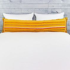 a bed with white sheets and pillows on top of it in front of a wooden wall