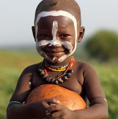 a young boy with white paint on his face and chest, standing in front of green grass