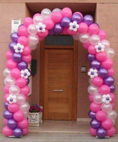 an arch made out of balloons with flowers on it in front of a building entrance