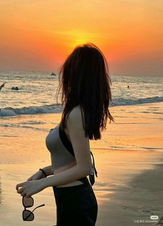 a woman standing on top of a beach next to the ocean at sun set with her hair blowing in the wind