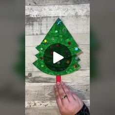 a hand holding a green paper christmas tree on a red toothpick with the video below it