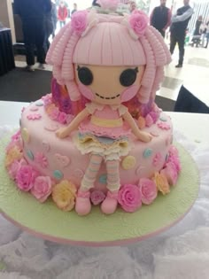 a pink cake with a doll on top and flowers around the edges, sitting on a table