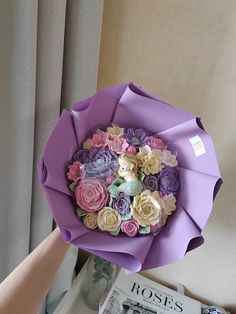 someone is holding a bouquet of flowers in front of a book on a table next to a window