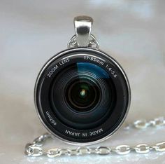 a camera lens necklace is shown on a white surface with a chain attached to it