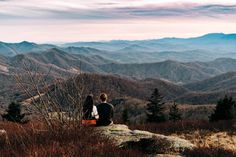 two people sitting on top of a mountain looking at the mountains