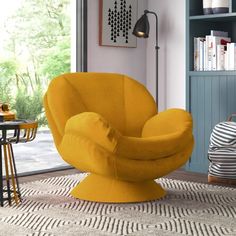 a yellow chair sitting on top of a rug in a living room next to a book shelf