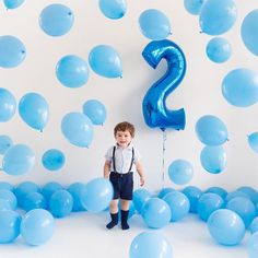 a young boy standing in front of balloons with the number 2 on it's side