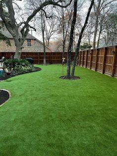 a backyard with artificial grass and trees in the back yard, surrounded by wood fence