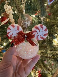 hand holding mickey mouse ornament in front of a christmas tree with red and white decorations