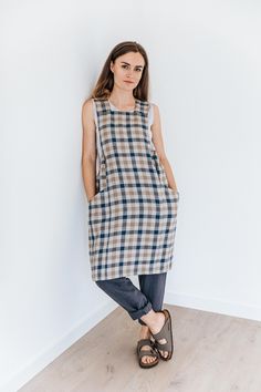 a woman standing in front of a white wall wearing a plaid shirt and blue jeans