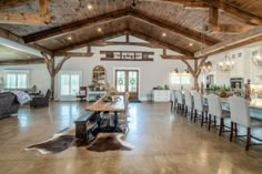 a large open living room and dining area with wood beams on the ceiling, high ceilings, and white chairs