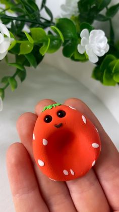 a hand holding a small orange toy with white dots on it's face and eyes