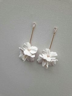 two white flowers are hanging from hooks on a gray surface, one is gold and the other is silver