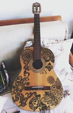 a wooden guitar sitting on top of a bed next to a pen and pencils