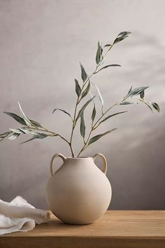 a plant in a white vase sitting on a wooden table next to a cloth and napkin