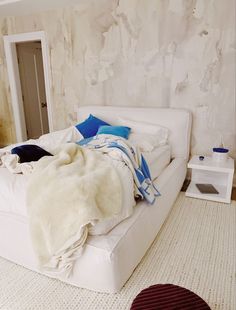 a white bed sitting in a bedroom next to a wall with peeling paint on it