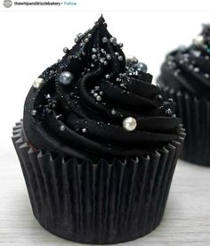 two cupcakes with black frosting and sprinkles sitting on top of each other