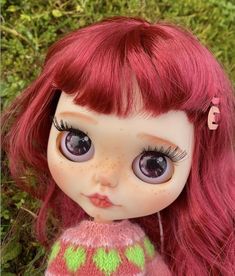 a close up of a doll with long red hair and big eyes wearing a sweater