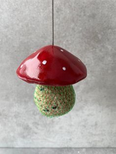 a green and red mushroom ornament hanging from a string on a gray wall