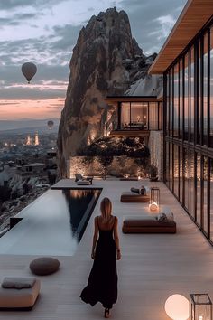 a woman in a long black dress is walking towards a pool and hot air balloons