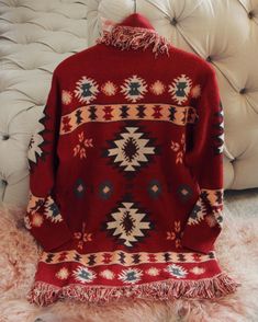 a red sweater sitting on top of a fur rug next to a white chair and ottoman