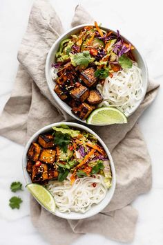 two bowls filled with noodles and vegetables on top of a white table cloth next to a napkin