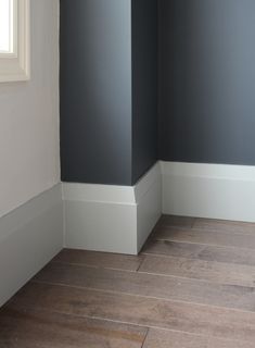 the corner of a room with gray walls and white trim on the wood flooring