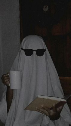 a person dressed as a ghost reading a book and holding a coffee cup