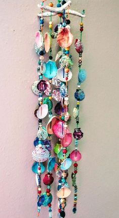 a colorful wind chime hanging on the wall next to a white vase with flowers and seashells